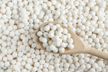 White dry tapioca pearls in wooden spoon on tapioca background. Top view of raw tapioca starch balls used for bubble tea or desserts. Tapioca pearls as healthy gluten free ingredient.