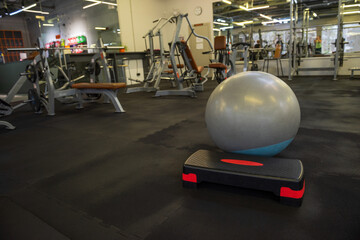 Fitness equipment in a gym interior. A stability ball placed on a step platform in a modern fitness center with workout machines in the background.