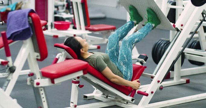 A middle-aged woman trains her leg muscles with the leg press machine. She strengthens her legs using the leg press, maintaining proper form and steady pace to maximize muscle engagement in the gym.