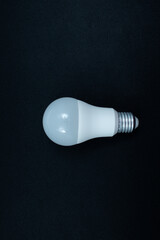 A modern, white LED light bulb with a standard screw base on a solid black background. Perfect for concepts of power, ideas, and sustainability.  Presented in the center of horizontal picture.