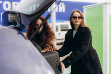 Young women packing luggage into car trunk for road trip