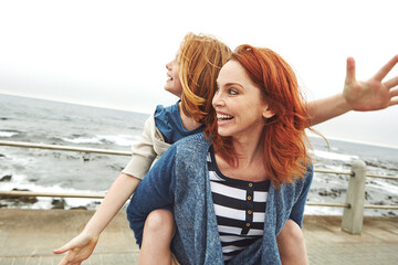 Piggyback, love and girl with mom for beach, freedom or fun together for bonding. Family, ocean and mother with daughter on holiday outdoor with smile, flying game and travel for weekend or vacation