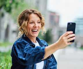 Portrait of a young woman girl taking a selfie with a smartphone mobile phone , having fun and laughing, walking city street