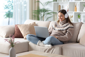 Fototapeta premium Happy woman wearing headphone in winter watching media
