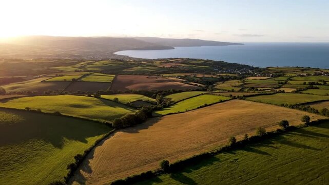 Aerial view of a picturesque countryside landscape with fields, coastline, and ocean during golden hour sunset