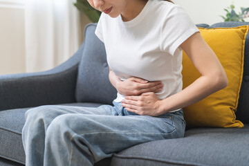 Sick asian young woman in pain, hand holding belly, stomach pain from food poisoning, girl hurt...