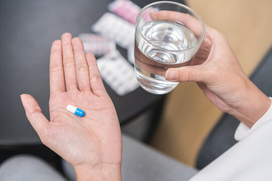 Sick, asian young woman, girl hand holding pill capsule, painkiller medicine from stomach pain, head ache, pain for treatment, take drug or vitamin and glass of water at home, pharmacy and health care