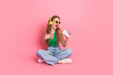 Stylish young woman enjoying music and capturing moments with her smartphone against a vibrant pink...