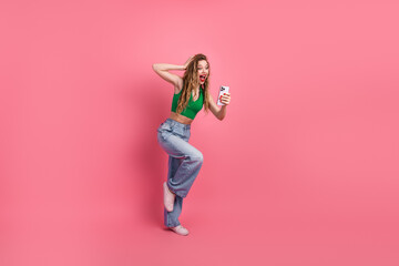 Joyful young woman with stylish outfit posing with her phone against a vibrant pink background