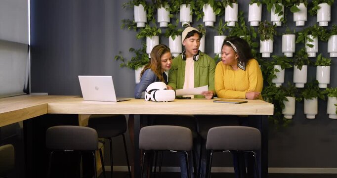 Diverse coworkers retrieving spec sheet at lounge while examining VR headset and discussing design
