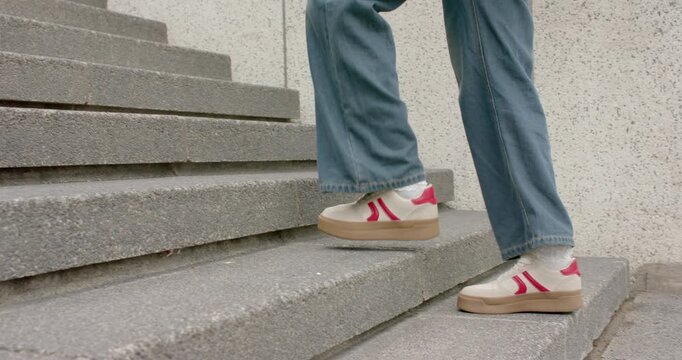 Stepping onto first step red-shoed walker ascending stairs toward person with coffee cup and pack