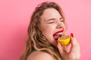 Young stylish woman enjoying a playful moment with a sliced lemon against a vibrant pink background