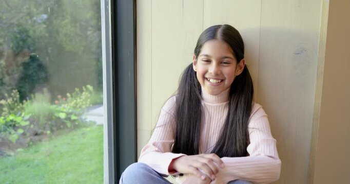 Indian girl smiling at camera on window bench then spotting garden shifting gaze to admire greenery