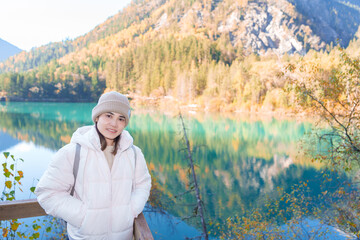 Fototapeta premium Happy woman traveler travel in jiuzhaigou national park in Sichuan, China. Tourist sightseeing Arrow Bamboo lake and snow mountain in Autumn season. Famous Landmark and Vacation near Chengdu, China
