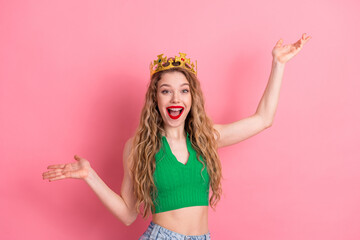 Cheerful young woman with a golden crown and arms spread, expressing fun and style against a bright...