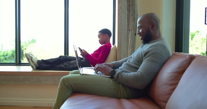 African American son presenting smartphone and father repositioning laptop sharing screen at home