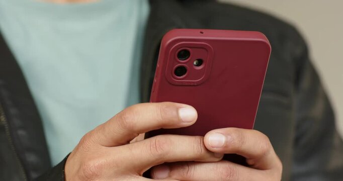 Man is placing thumbs on red smartphone in room, tapping right corner to scroll, check notification