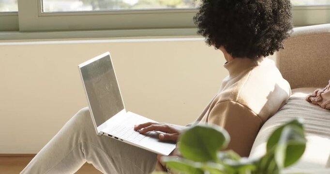 Steadying laptop on lap near window, person is typing keys and glancing outside for work