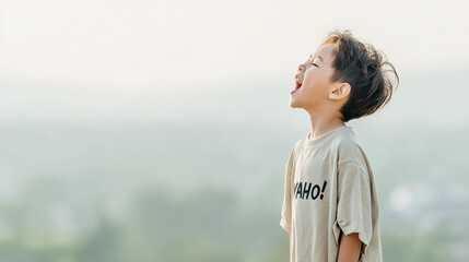 日本人の幼い少年が明るい屋外で、顔を空に向けて、大きな口を開けて大声で叫んでいる瞬間を捉えた横顔のポートレート。Tシャツには「YAHO!」と書かれており、喜び、自由、開放感の感情を表現。背景は霧がかったような柔らかい緑、崖の上