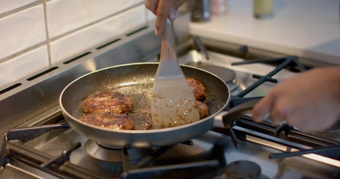 Pan heating on burner is sizzling beef patties; cook is turning, basting with spatula for sear