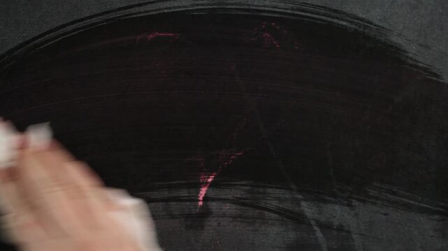 A pink heart is drawn with chalk on a chalkboard, then erased with a rag. Good for representing love, relationships, and Valentine's Day themes.
