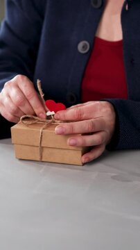 A person prepares a gift for someone special by tying a string around a box with a heart tag. This shows the effort put into making a heartfelt present for Valentine's Day.