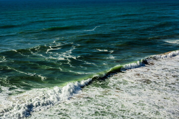 Powerful ocean waves crash against the shore, creating white foam and a dynamic coastal scene, evoking nature, energy, and sea movement.