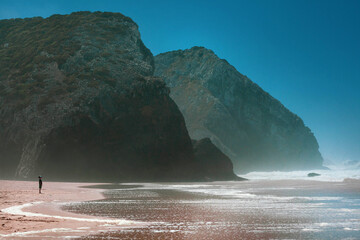 Silhouette of a boy watching powerful waves crash against dramatic coastal rock formations, creating a striking seaside landscape scene.