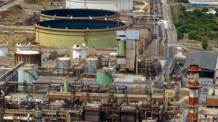 Fototapeta premium A close-up aerial view of the dense, intricate machinery of a refinery. The scene is dominated by interconnected metal structures, distillation columns, pipes, and walkways.