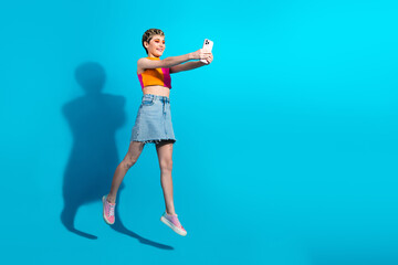 Young woman jumping taking selfie against blue background in casual summer fashion