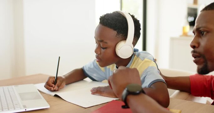 African American father and son practicing writing in notebook after pointing at trackpad at home