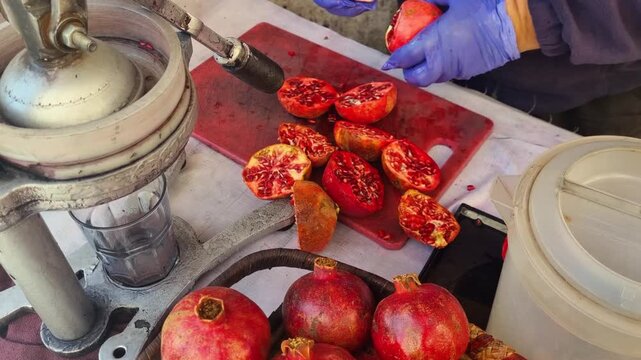 Close-up of a gloved vendor cutting fresh pomegranates outdoors in Madaba&rsquo;s old town on a sunny day preparing the fruit for a healthy juice drink