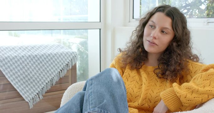 Glancing through window, woman leaning on hand for reflection, smiling on sofa at home, copy space