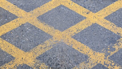 Yellow lines intersect on the concrete parking lot. This traffic marking indicates a no-parking zone, hazard area, safety, and traffic regulations. Realistic texture and slightly faded paint.