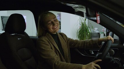 Smiling woman sitting in a new car and looking at the camera in the showroom