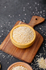 Quinoa seeds in multiple wooden bowls and spoons on dark background
