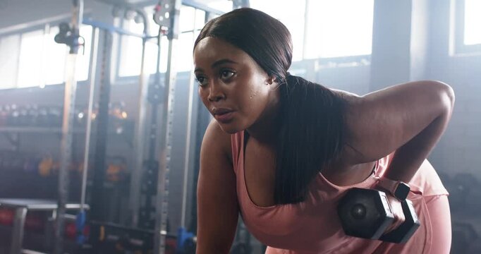 Steadying on bench, African American woman gripping dumbbell and rowing for strength in weight room