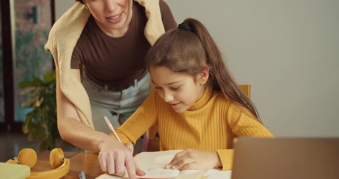 Mother assists daughter with schoolwork in cozy kitchen environment