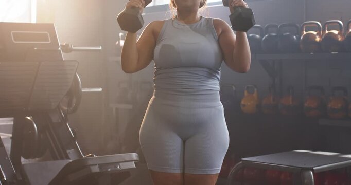 African American woman in grey gear at gym lifting dumbbells pressing overhead boosting strength