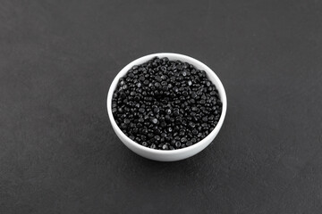 Black polyethylene granules or masterbatch in white ceramic dish. Uniform pellets dyed with carbon black pigment. Granulated plastic polymer