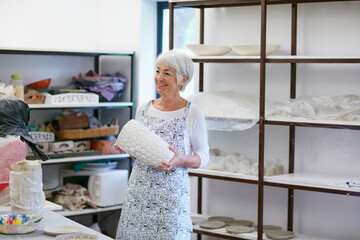 Ceramic, happy and senior woman in workshop for pottery design, diy hobby and shelf for sculptures. Retirement, art studio and elderly person with vase for handicraft, learning skills and creative