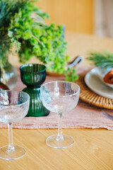 Two clear cocktail glasses with green vase and plant on wooden table with pink cloth