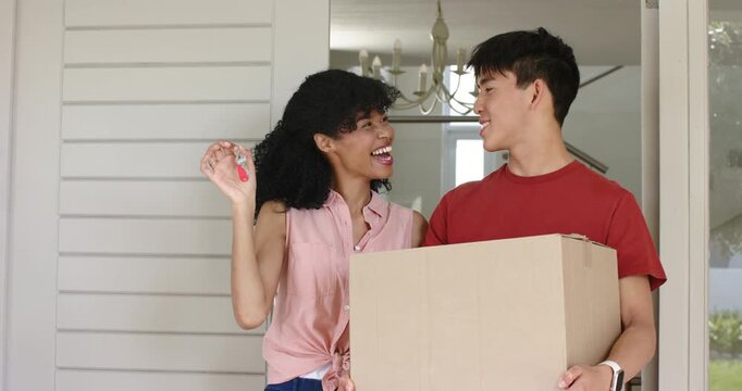 Asian man and African American woman stepping on porch jiggling red keys holding box unlocking door