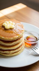 A stack of golden-brown griddle cakes on a white plate, topped with a paw-shaped butter pat and syrup. A small glass of syrup and a fork are next to them