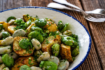 Boiled broad bean with baked potatoes in bowl on wooden table
