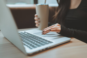 Woman working on laptop in cozy cafe while holding a drink reusable cup, modern lifestyle and remote work concept with casual productivity mood