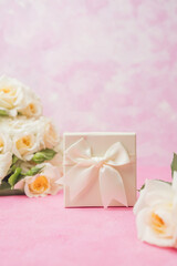 Closeup of elegant white gift box with satin ribbon and rose bouquet