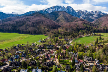 Aerial panoramic view of the Strążyska Valley near Zakopane, Poland, showcasing the distinctive Giewont mountain peak and residential areas surrounded by lush green forests in the Tatra Mountains.
