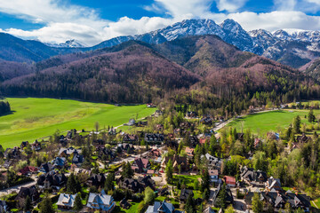 Aerial panoramic view of the Strążyska Valley near Zakopane, Poland, showcasing the distinctive Giewont mountain peak and residential areas surrounded by lush green forests in the Tatra Mountains.