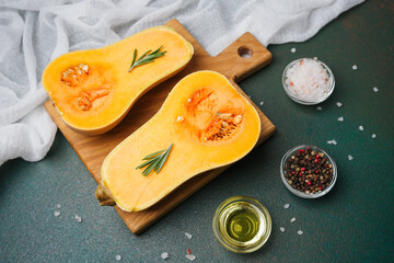 Halved butternut squash with rosemary, pepper, salt, and oil on a cutting board, dark background